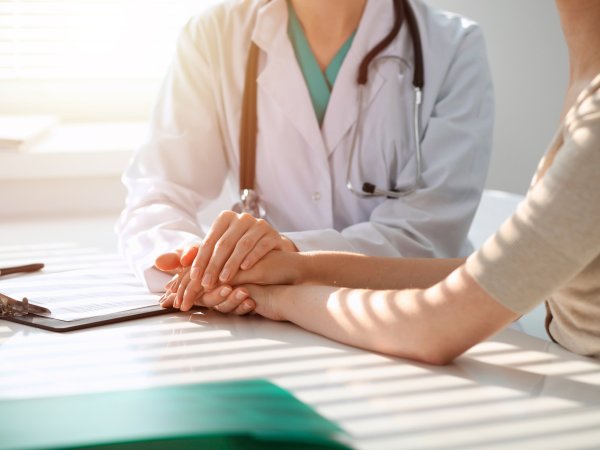 Un médico sostiene la mano de un paciente, mostrando apoyo y empatía en un entorno clínico.