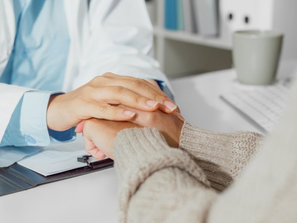 Un médico sostiene las manos de un paciente, simbolizando apoyo y empatía.