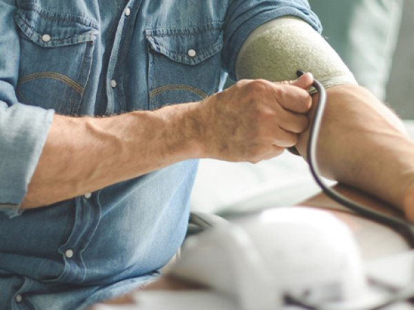 Hombre apoyado en un escritorio, realizando una medición de presión arterial.
